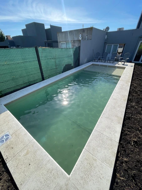 Piscina rectangular con borde atérmico junto a un cerramiento verde